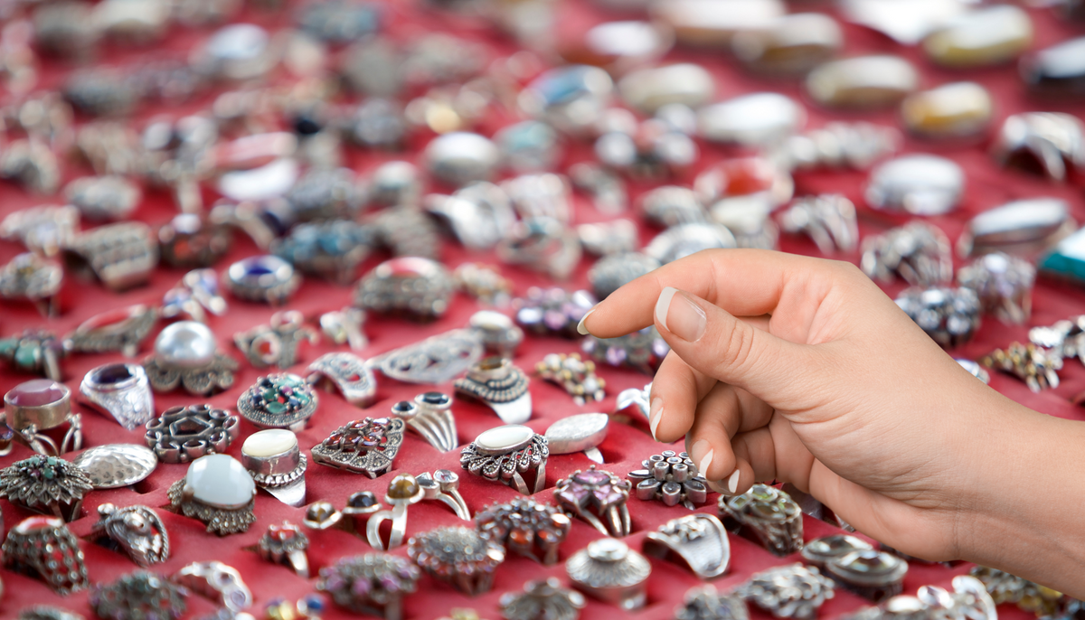 Hand reaching out to take a close look at a fashion ring on a red display tray