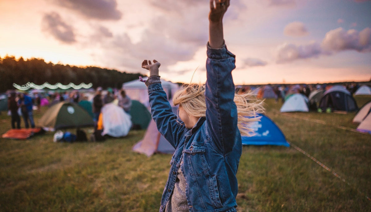 a woman in a music festival raising her arms in the air in front of tents