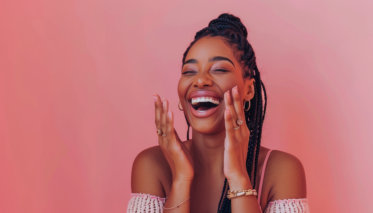 beautiful happy black woman with long hair in braids laughing and clapping on a pink background, wearing fashion rings and a pink off-shoulder top