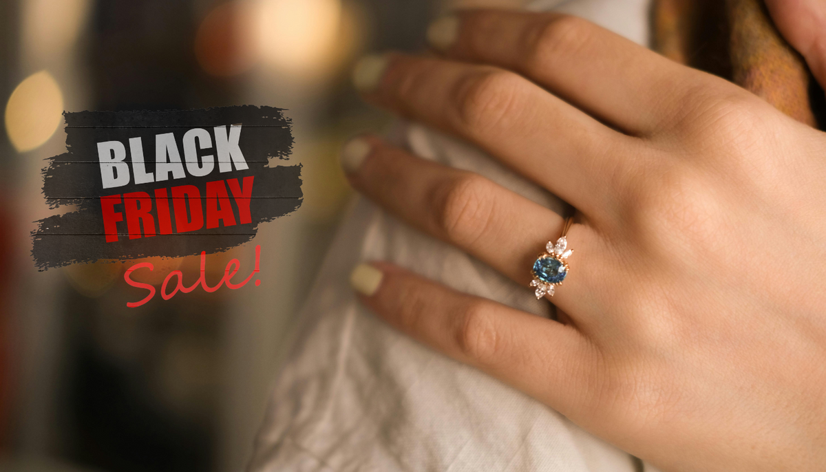 close up shot of a woman's hand on her shoulder wearing a fashion ring with a black friday sale sign in the background