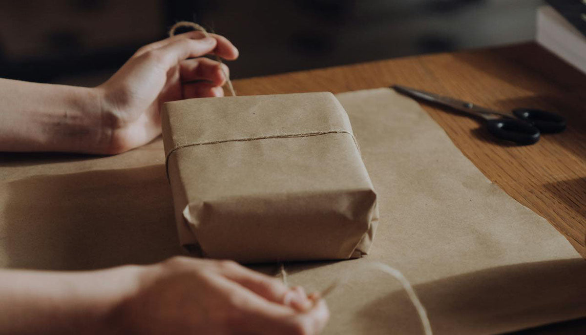 person's hands wrapping up a jewelry box with kraft paper