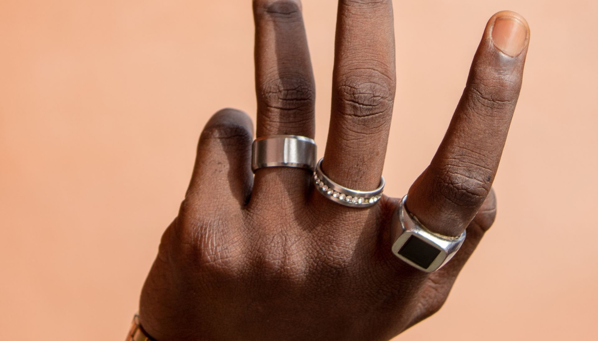 Close-up of a stylish hand adorned with rings and a gold watch against a beige backdrop, exuding luxury and minimalism