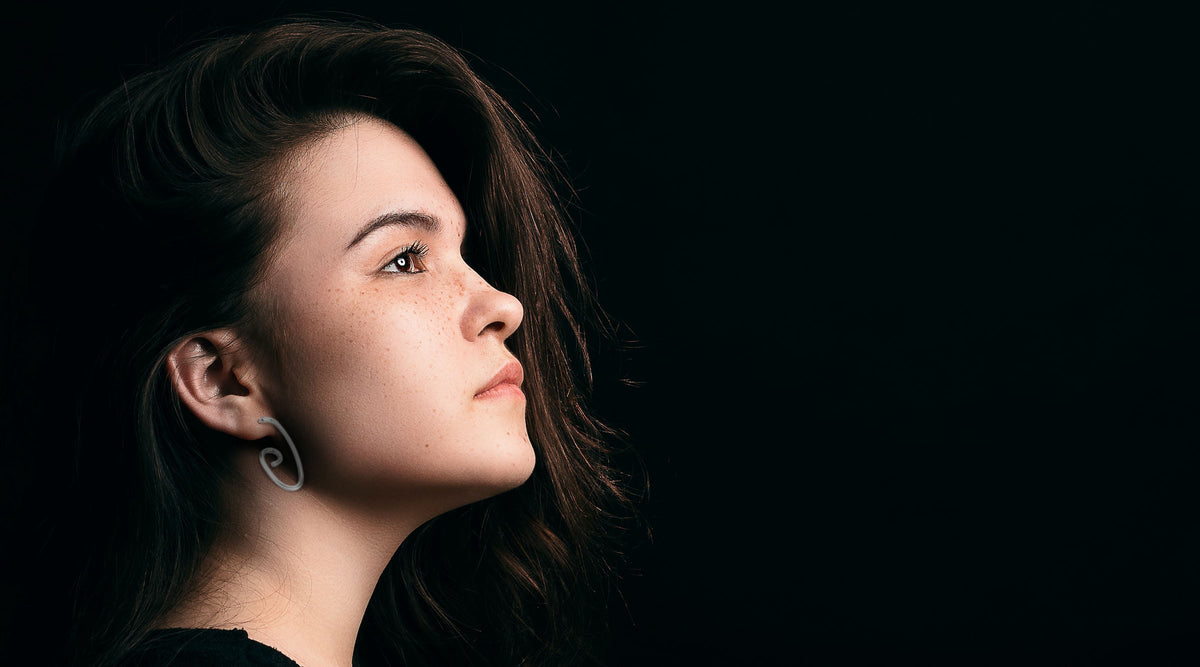 side profile of a beautiful brunette wearing minimalist swirl stainless steel earrings