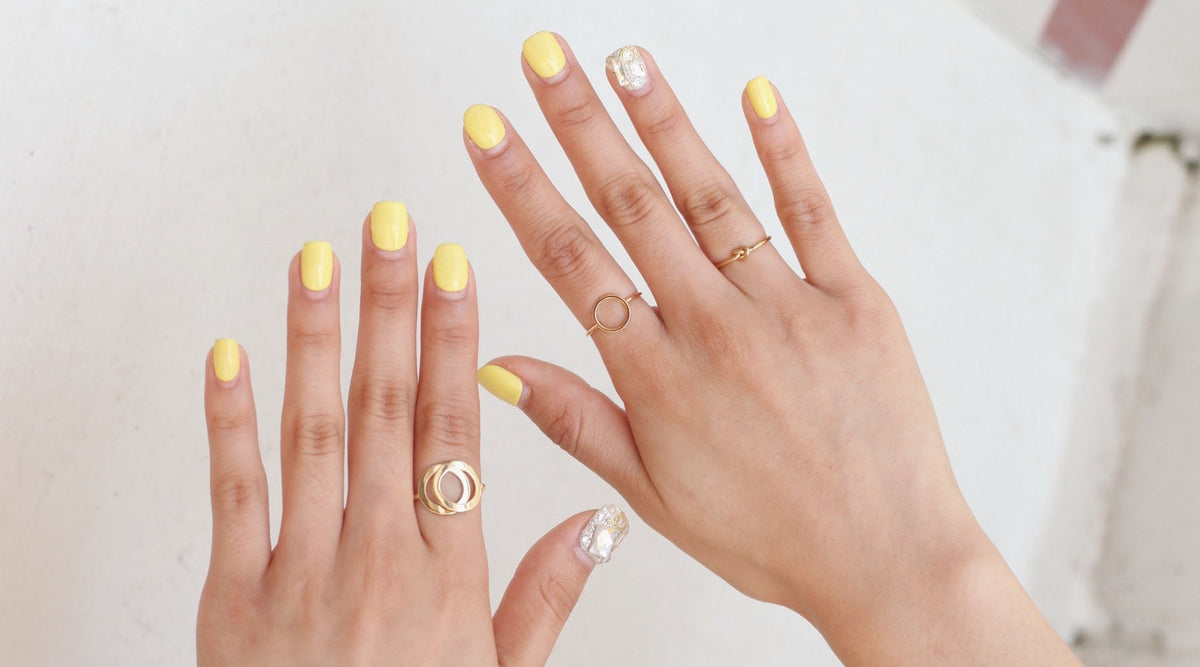 woman's hands with yellow nail polish wearing minimalist rings