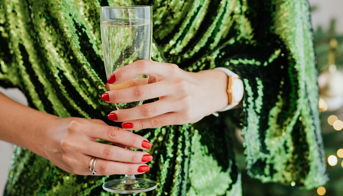 woman with red nails wearing fashion rings and a sparkly green dress holding a champagne glass