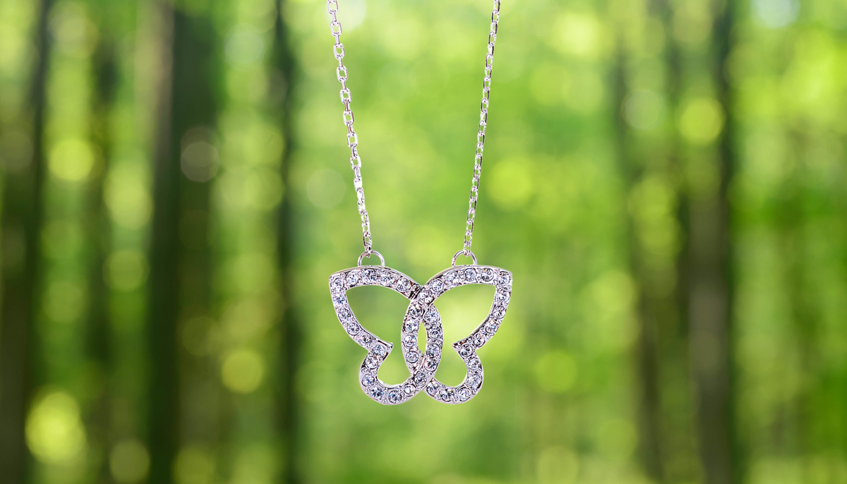 N7112 Fluttering Swarovski Crystal Elements Butterfly Rhodium Plated Necklace against a blurred forest background