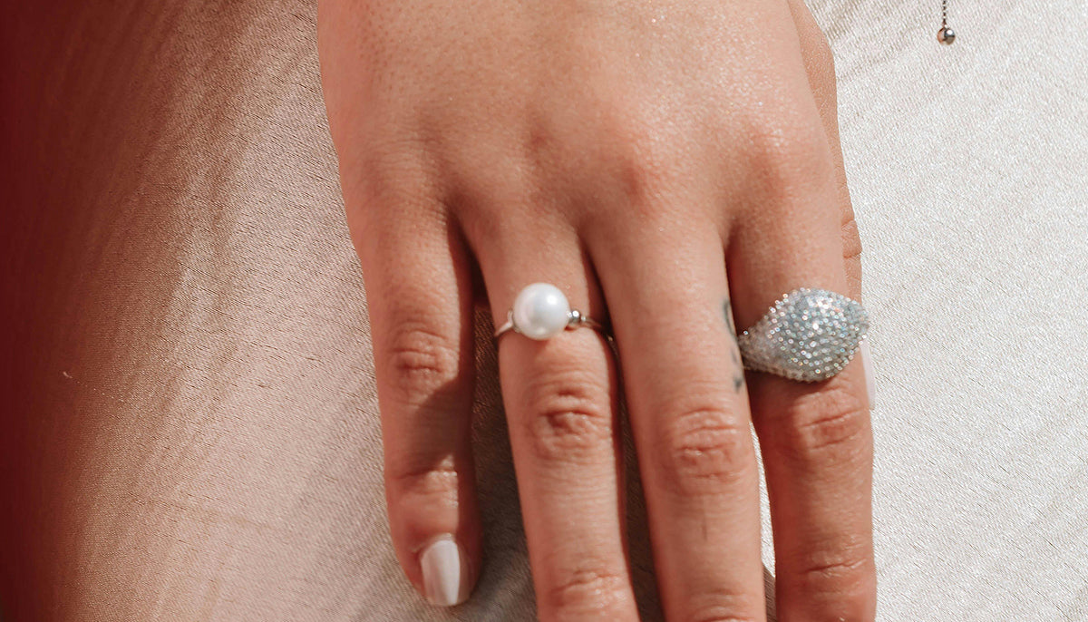 close up photo of a woman;s hand wearing a pearl fashion ring and a statement cz fashion ring