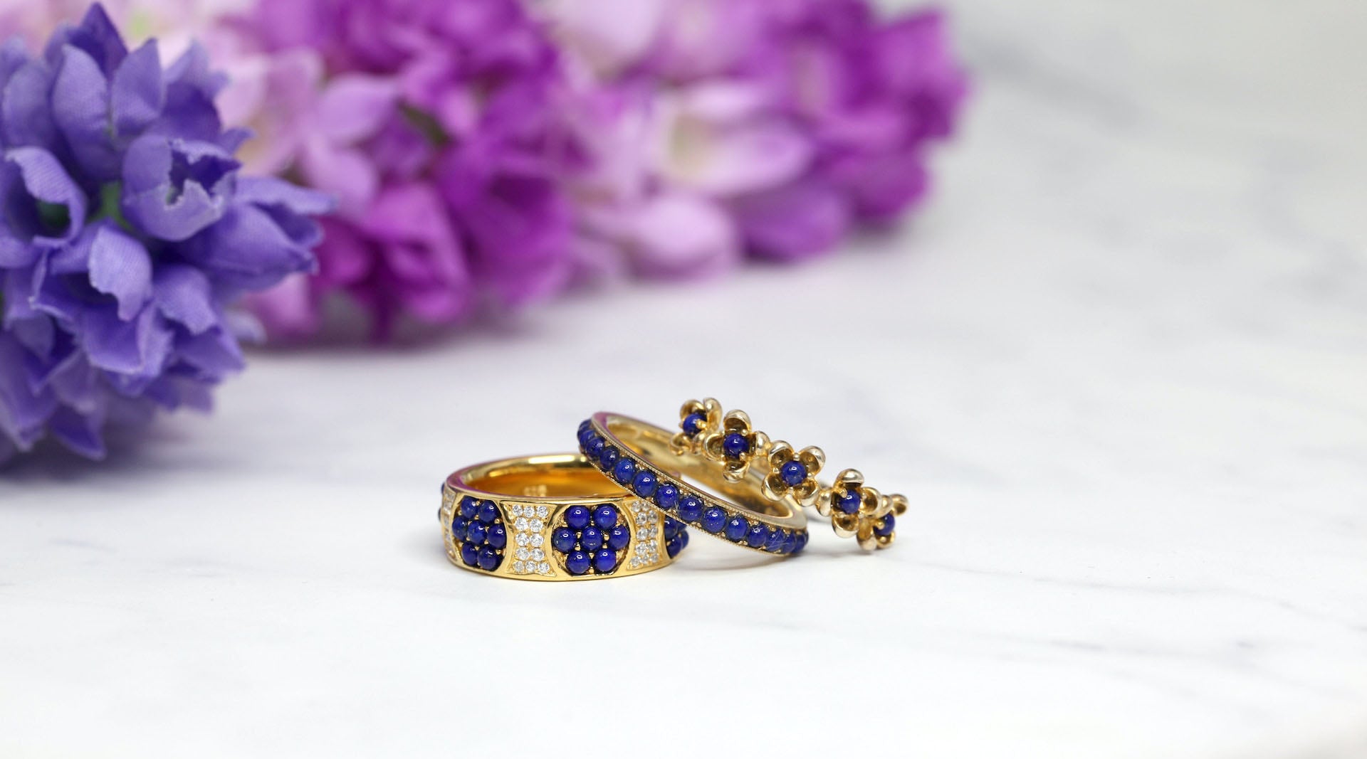 three gold-plated cz fashion rings on white surface with purple flowers at the background