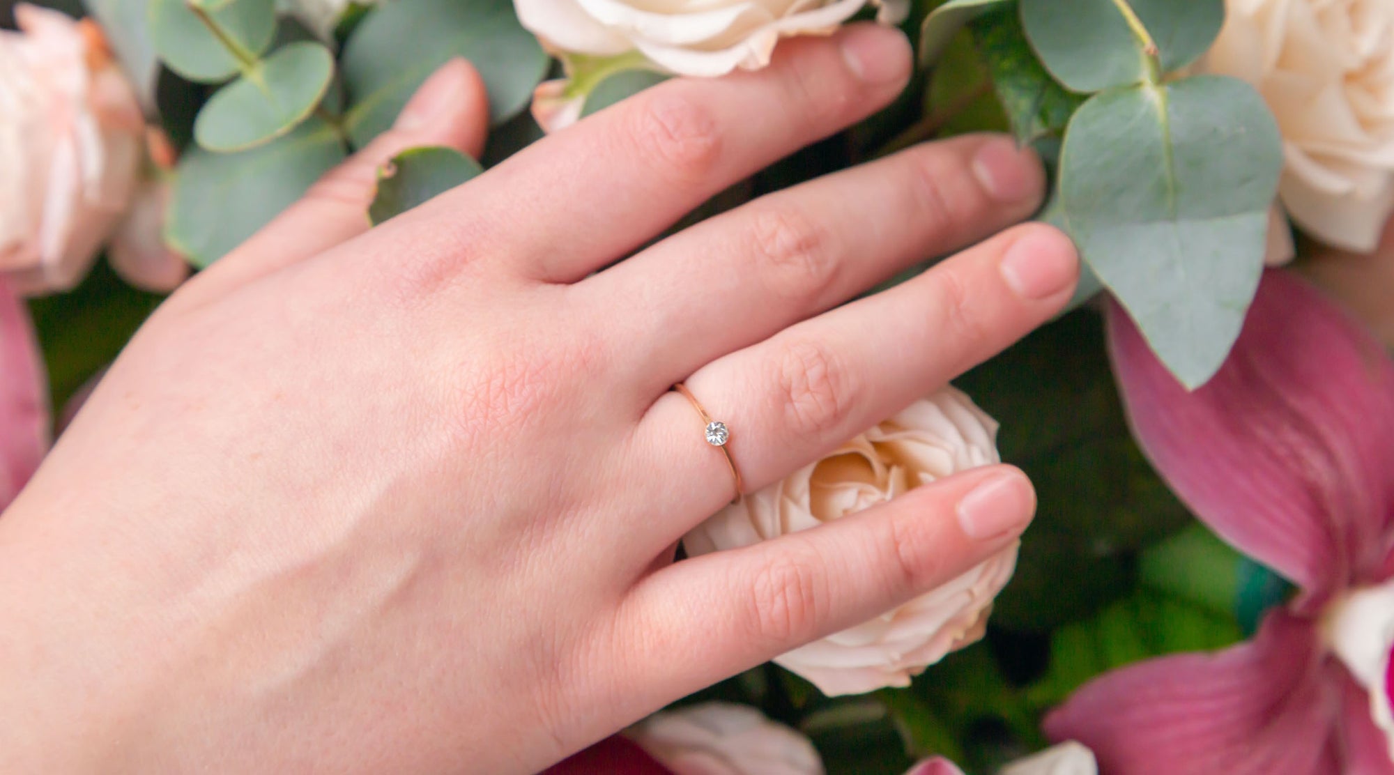 woman's hand on top of a bouquet of flowers wearing minimalist solitaire fashion rings