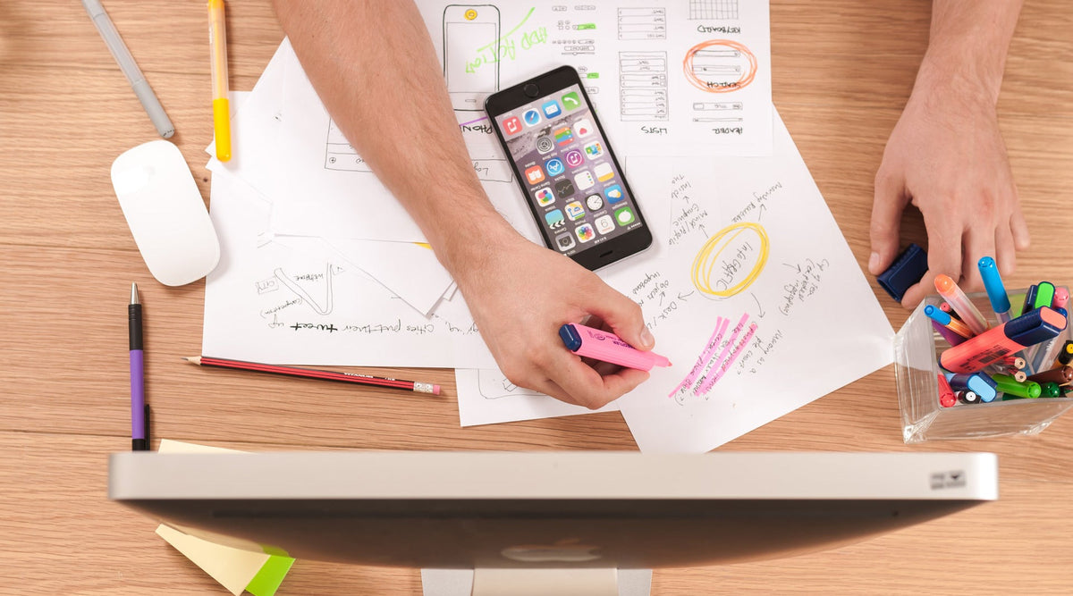 person writing on paper with smart phone and pc monitor in front of him