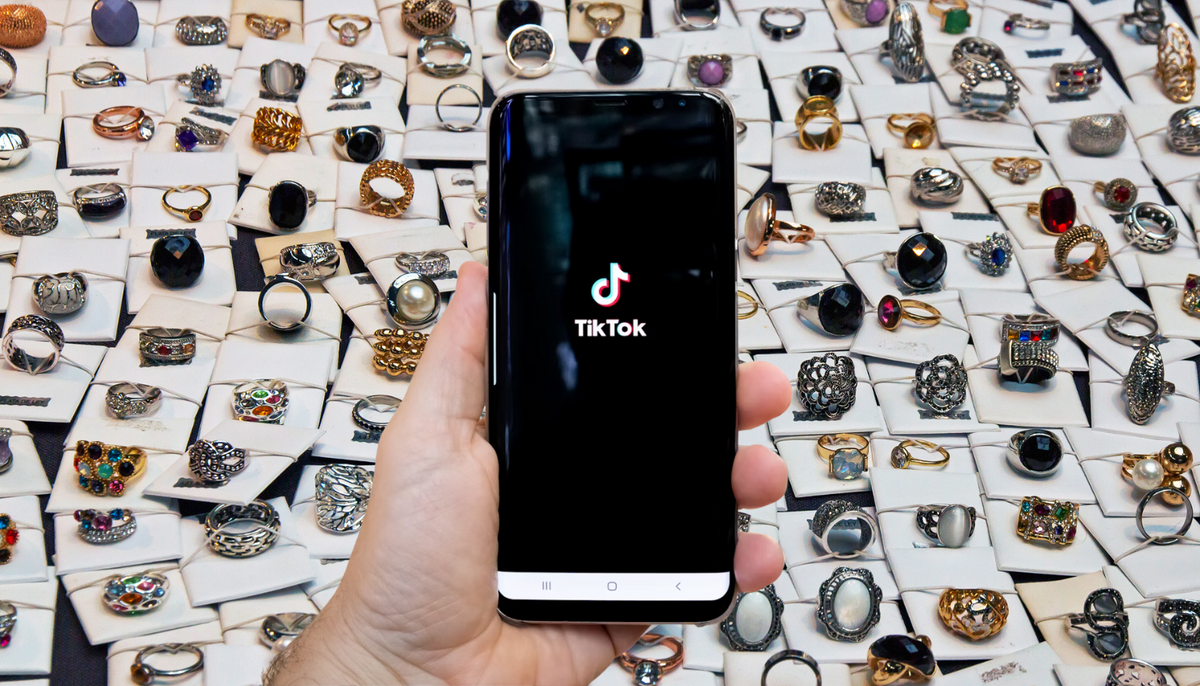 hand holding smart phone with tiktok logo on screen against a background of fashion rings on cards