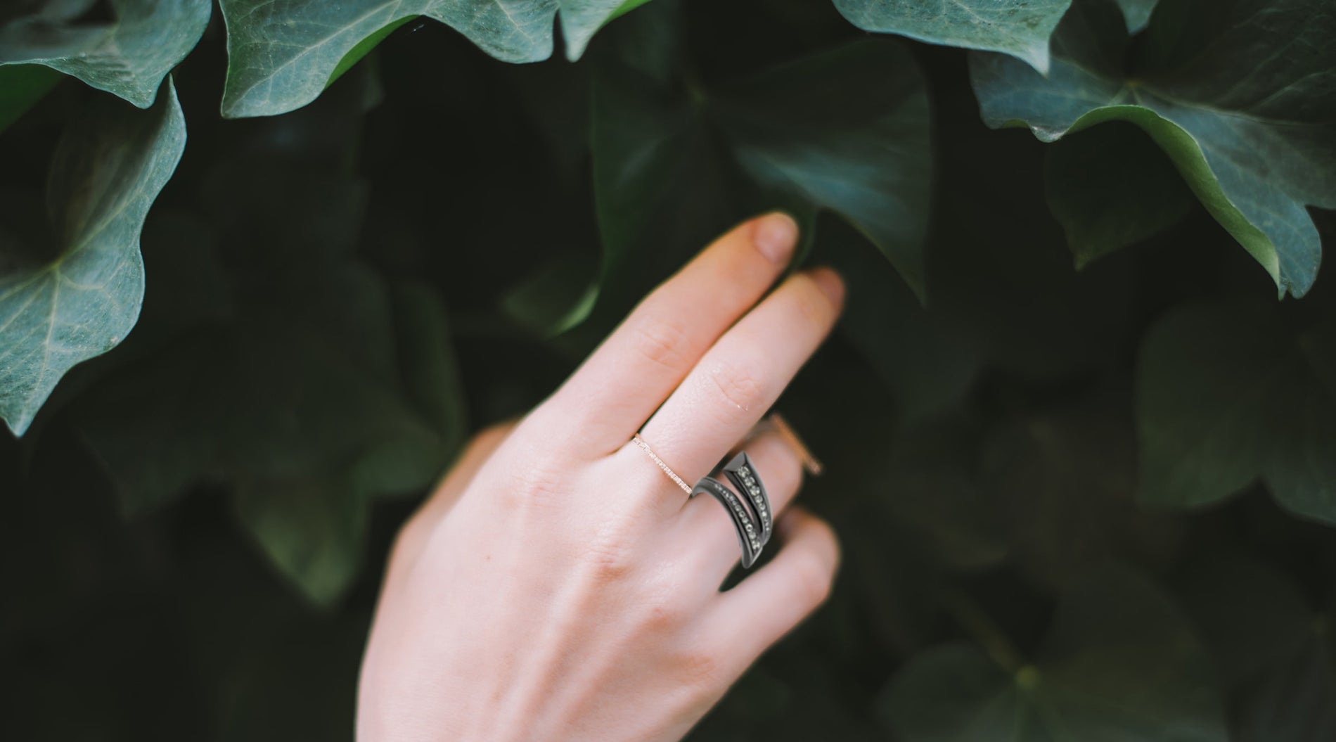hand touching leaves wearing gold ring and black plated fashion ring