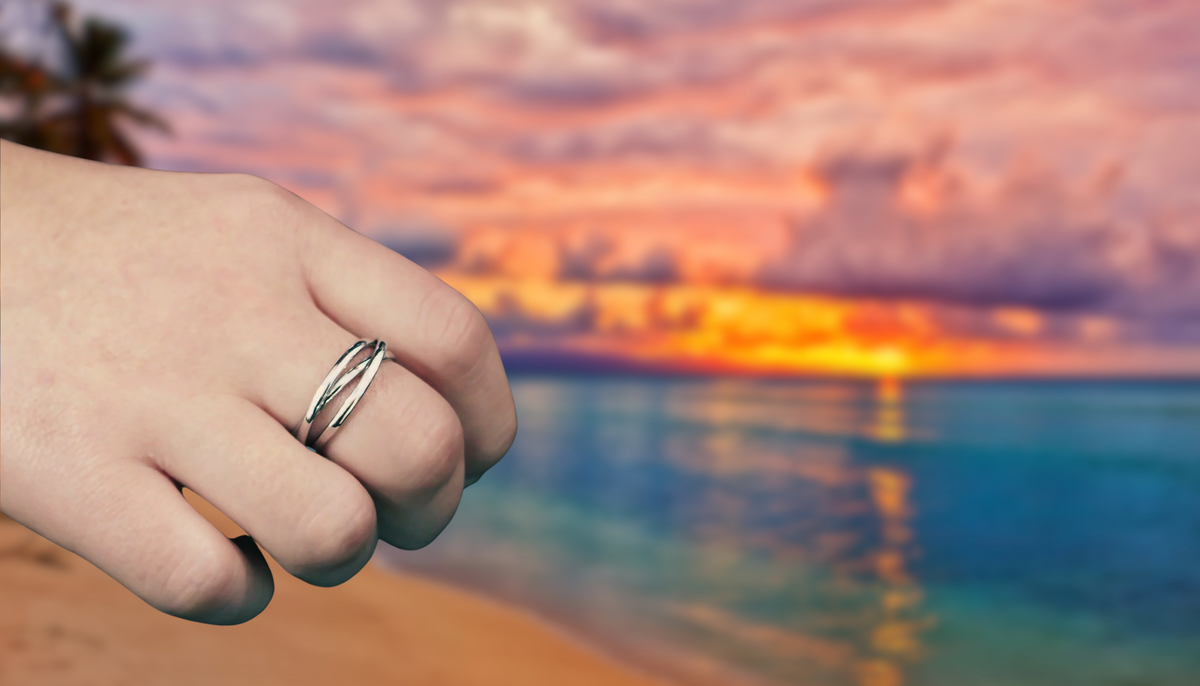 hand with Ceri Jewelry stainless steel fashion ring with blurred beach during sunset background