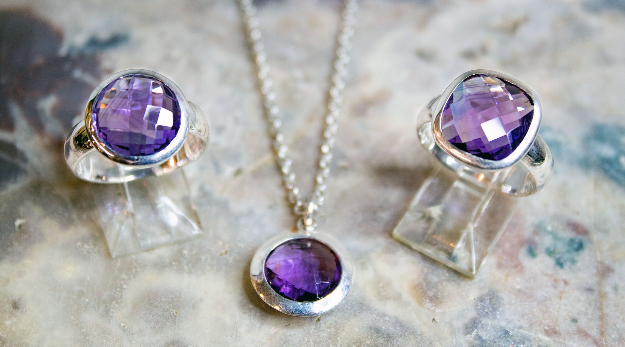 amethyst cz fashion rings and a pendant necklace on a marble surface