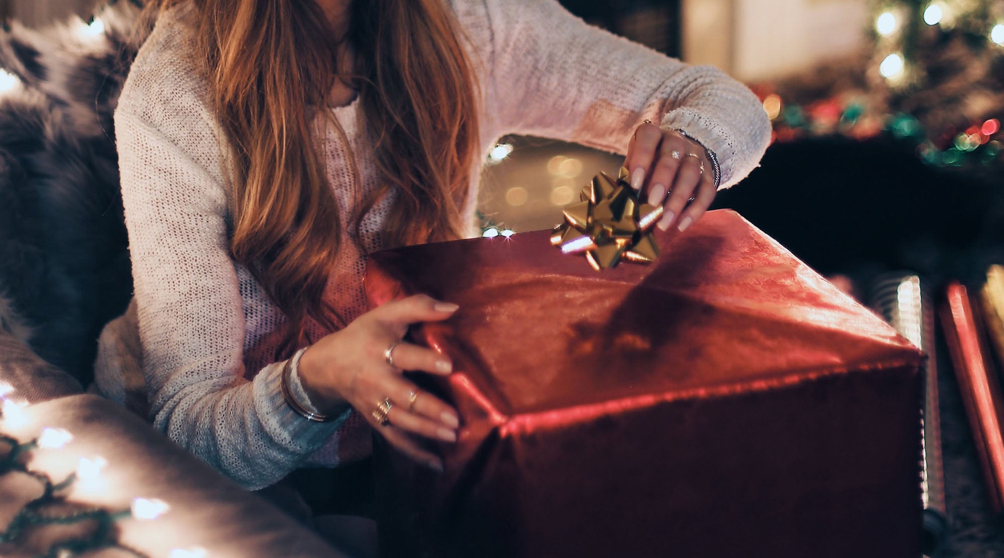 selective photo of red christmas gift about to be opened by woman wearing fashion rings