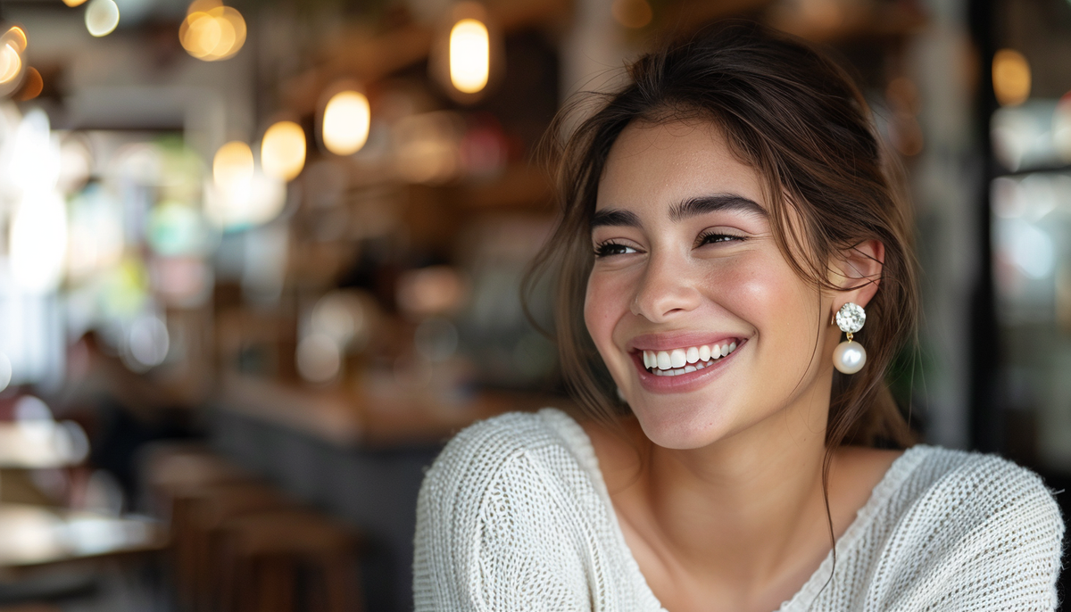 smiling brunette wearing pearl drop fashion earrings and a white knitted top with a beautiful bokeh background