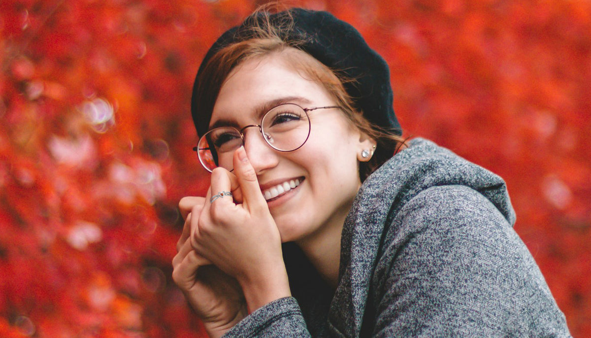 smiling woman in a sweater wearing a fashion ring with a rust orange crystal accent with the fall leaves on trees in the background