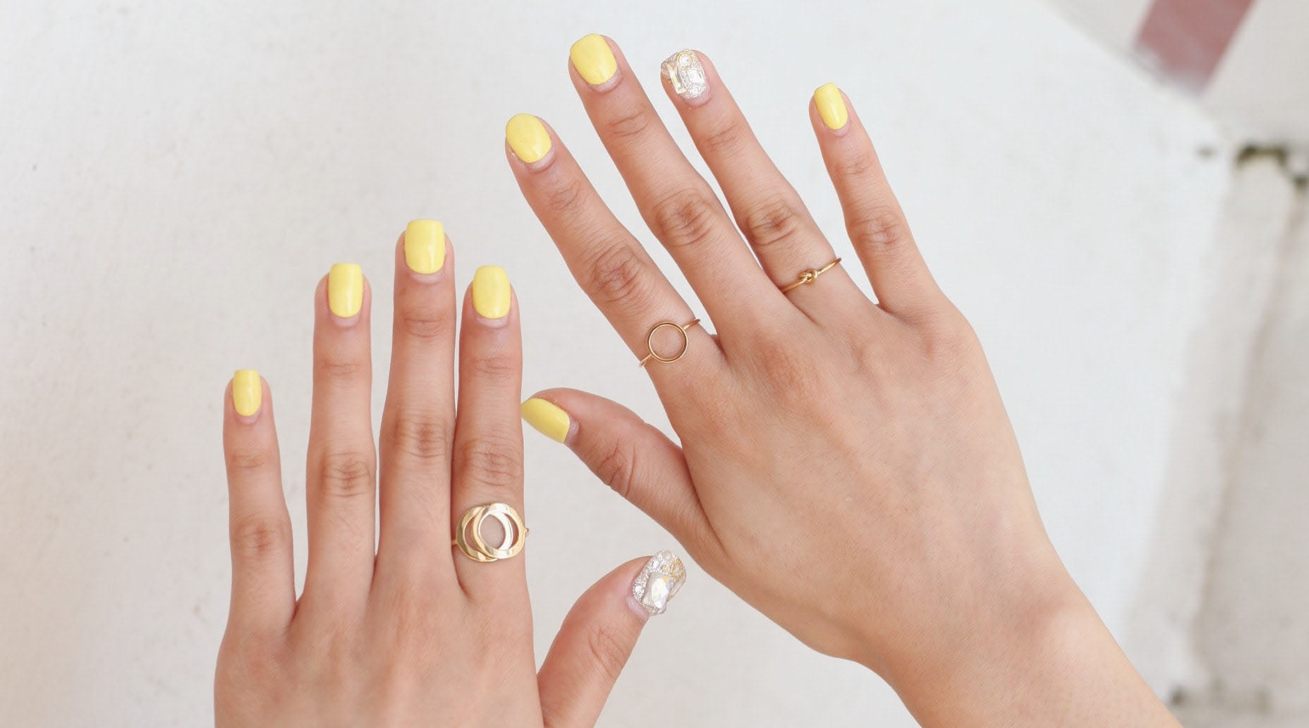 woman's hands with yellow nail polish wearing minimalist rings