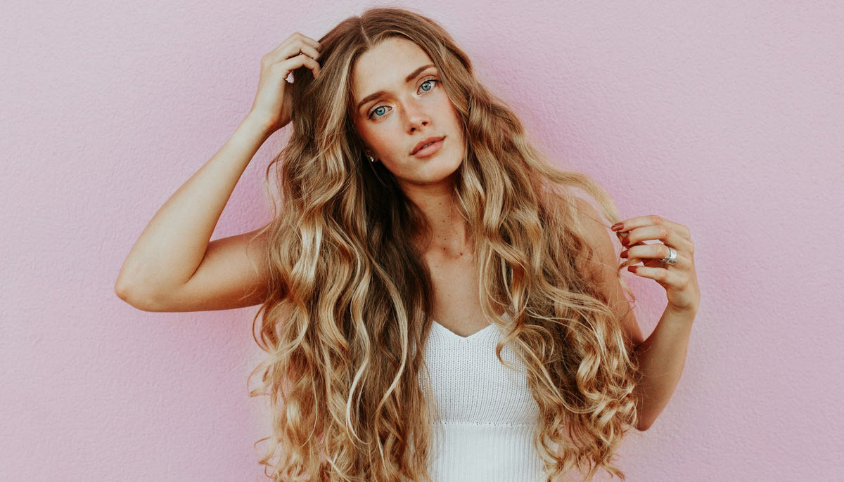 woman standing next to pink wall while scratching her head and wearing fashion rings