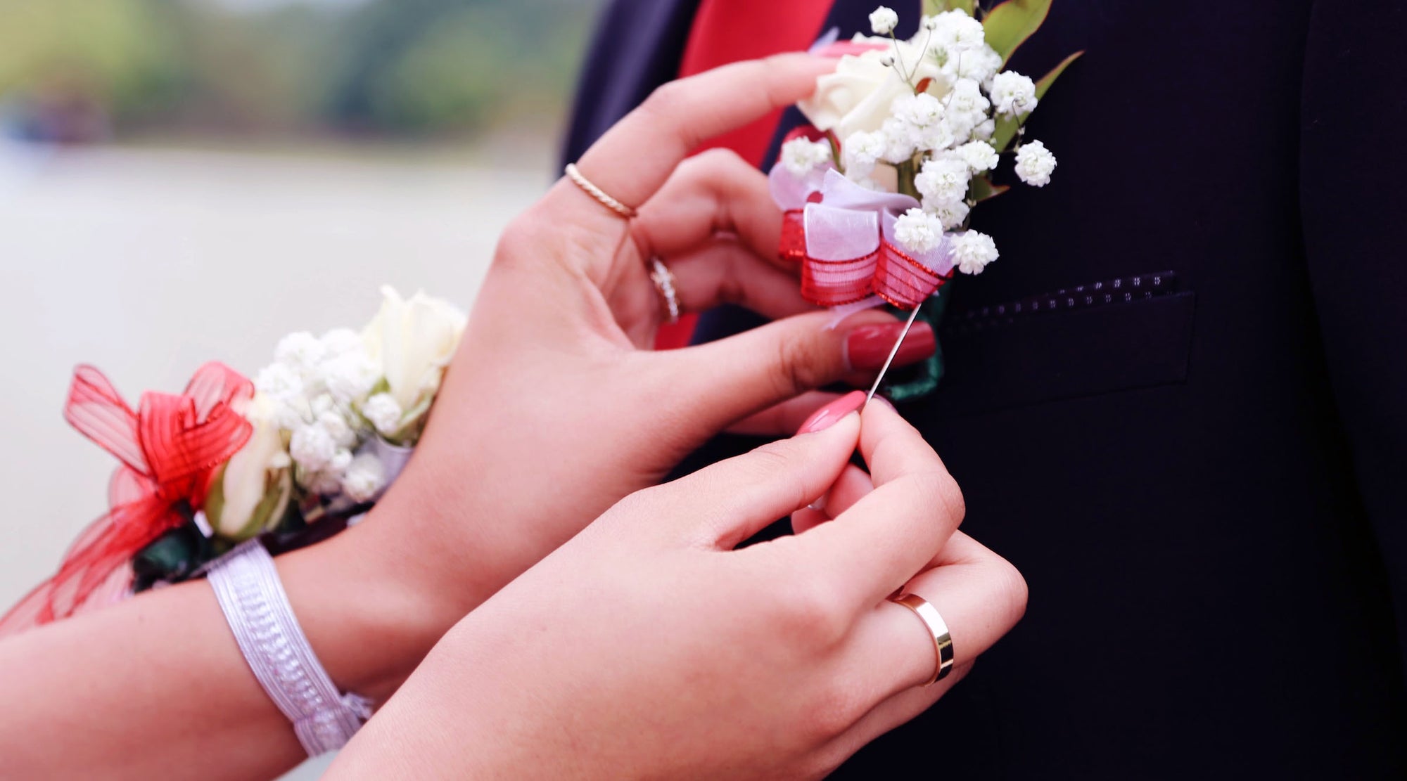 young lady wearing fashion rings attaching a flower pin to her prom date